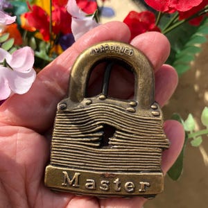 May include: A gold-toned padlock with the word "Master" engraved on the bottom. The padlock is labeled "Hardened" on the top.