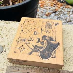 May include: Wooden stamp featuring a pirate design with a map, compass, and ship illustrations. The stamp measures approximately 3 inches in length and is made in the USA. The stamp is a craft supply.