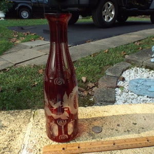 May include: A red glass vase with a cut glass design. The vase has a clear glass design of a bird and a tree.