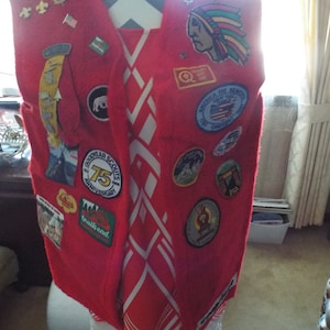 May include: Red felt vest with a white design and numerous patches, including a patch that says "Goodyear Scouts 75th Anniversary".
