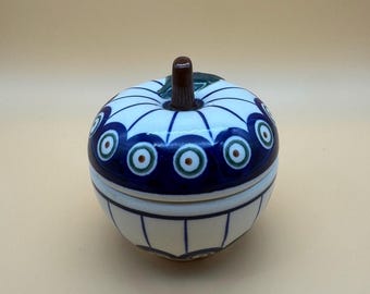 Könnte beinhalten: Eine keramische, apfelförmige Schmuckschatulle mit einem dunkelbraunen Stiel. Die Schachtel ist weiß mit einem blauen und grünen Muster an der Oberseite und den Seiten. Der Deckel hat einen dunkelblauen Rand mit kreisförmigen Designs.