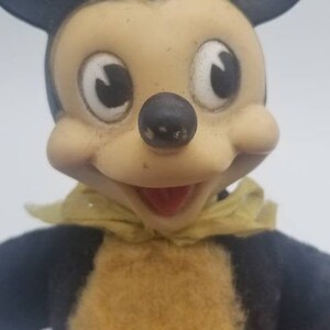 May include: A vintage plush Mickey Mouse toy with black ears, a black and white face, and a yellow bow tie. The toy has a brown fur chest and is wearing a black and blue outfit.