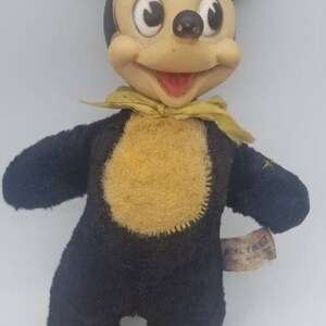 May include: Vintage Mickey Mouse plush toy with black fur, yellow felt accents, and a yellow bow tie. The toy has a tag that reads "Mickey Mouse".