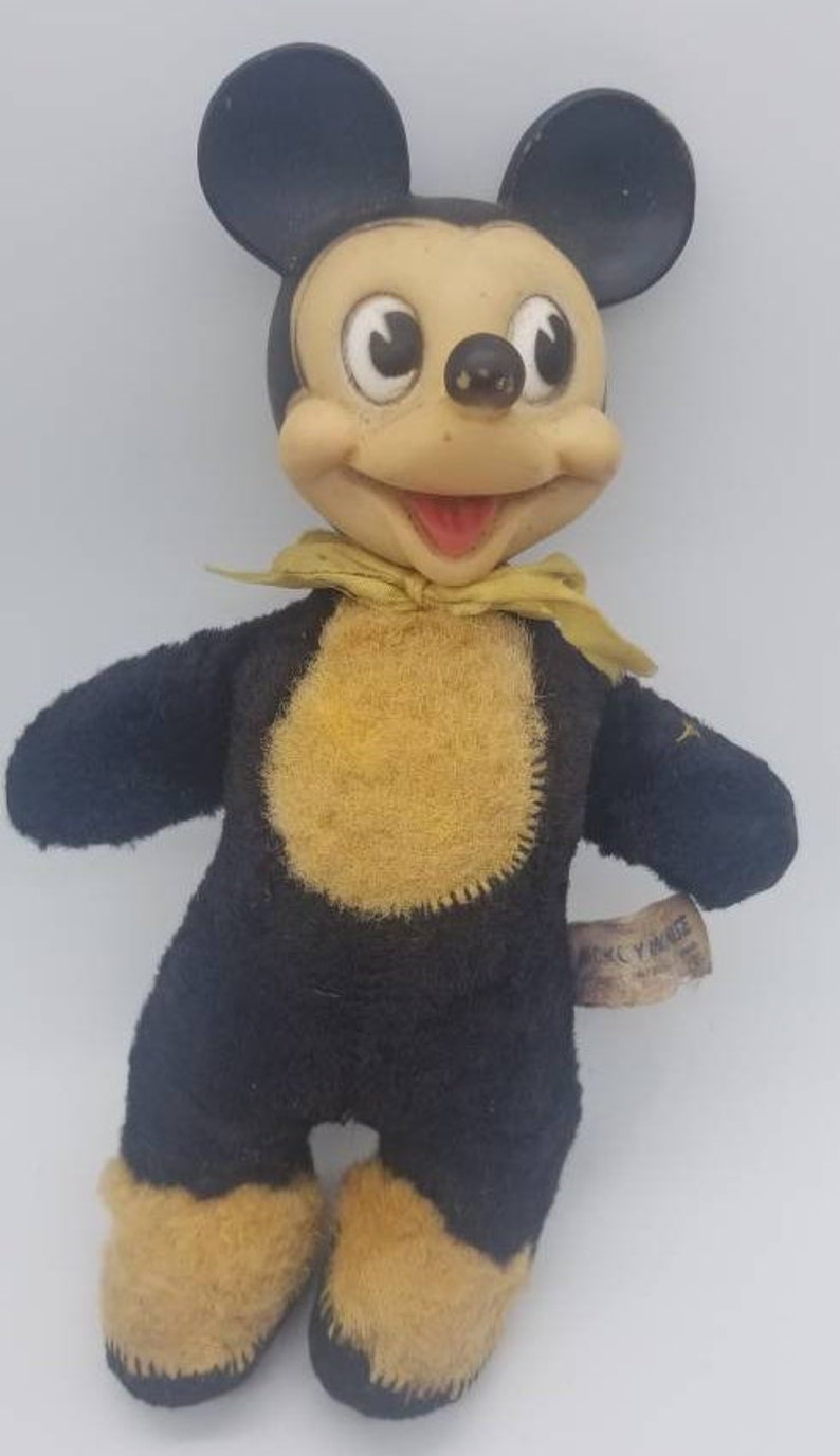 May include: Vintage Mickey Mouse plush toy with black fur, yellow felt accents, and a yellow bow tie. The toy has a tag that reads "Mickey Mouse".