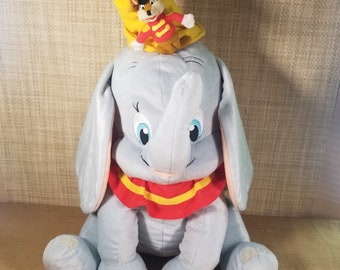 May include: A plush Dumbo the elephant toy with large ears, blue eyes, and a red and yellow collar. A small mouse wearing a red and yellow outfit and a yellow hat sits on top of Dumbo's head.