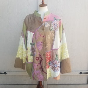 May include: Patchwork jacket with a mandarin collar and button closure. The jacket features a variety of fabrics in shades of brown, green, pink, and cream, with floral embroidery and applique details. The sleeves are long and wide.