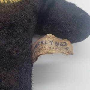 May include: A black and brown plush Mickey Mouse toy with a yellow fabric tag that reads "Mickey Mouse" and "Tall 18" in white text.
