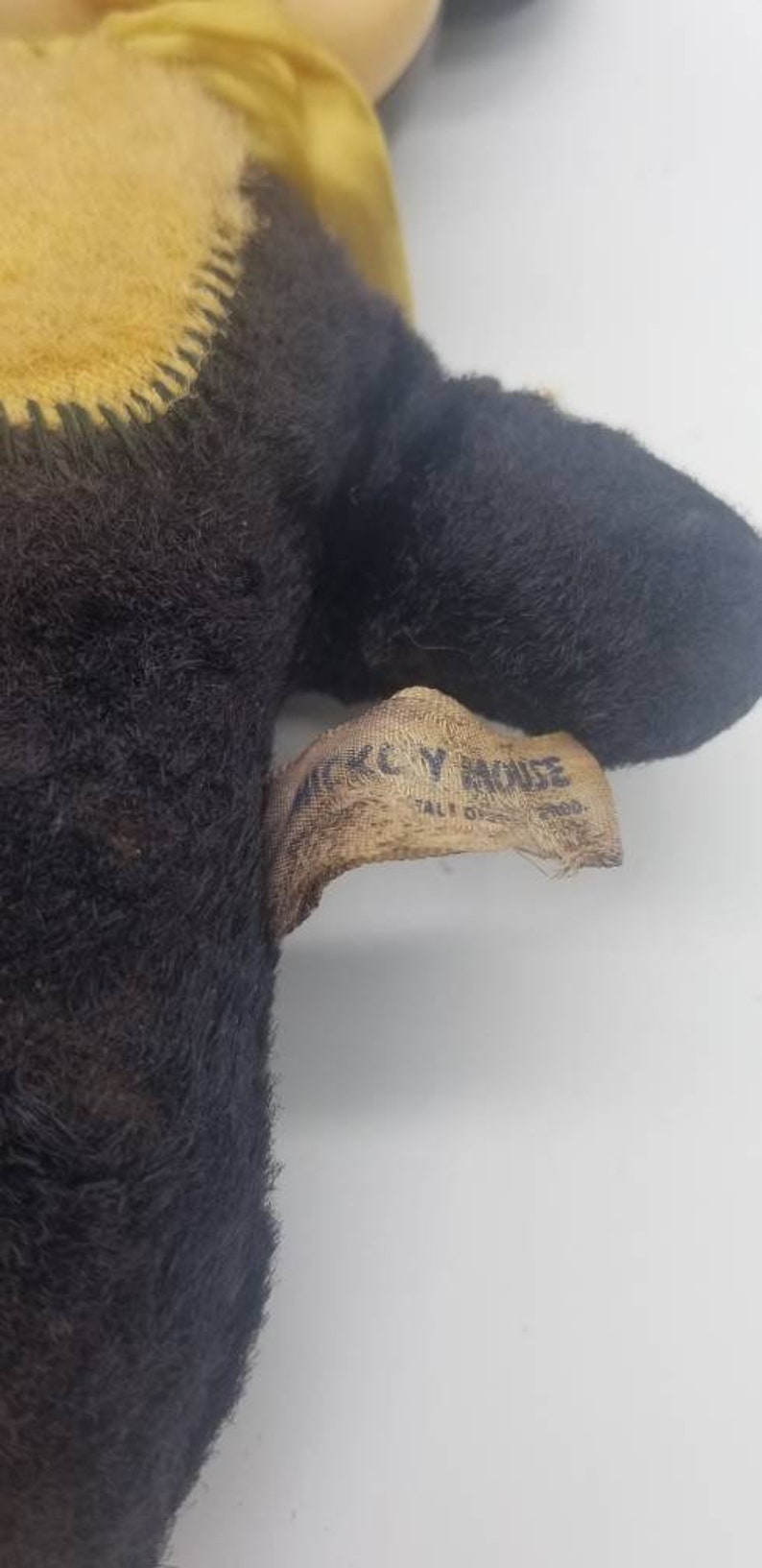 May include: A black and brown plush Mickey Mouse toy with a yellow fabric tag that reads "Mickey Mouse" and "Tall 18" in white text.