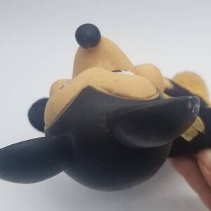 May include: A vintage black and yellow rubber Mickey Mouse toy. The toy is in a playful pose with its head tilted back and its ears sticking out.
