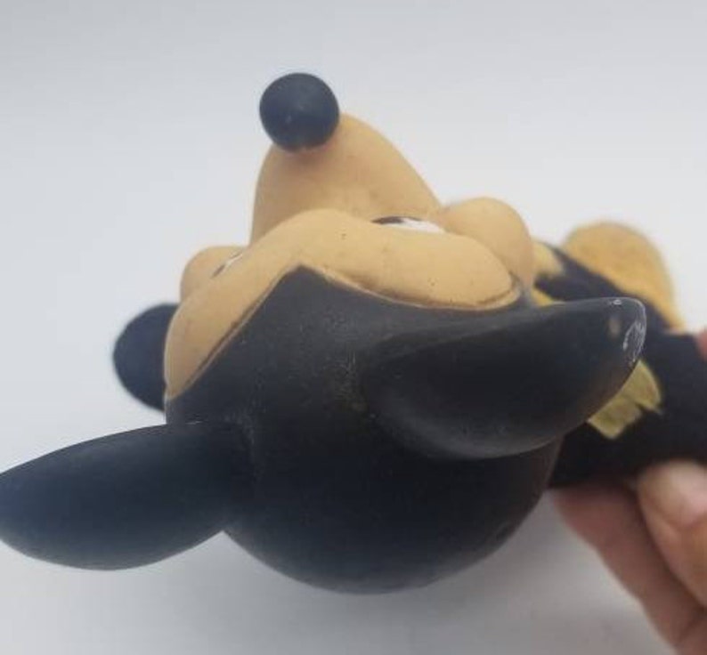 May include: A vintage black and yellow rubber Mickey Mouse toy. The toy is in a playful pose with its head tilted back and its ears sticking out.