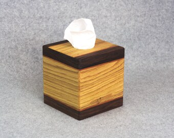 May include: A wooden tissue box cover with a dark wood trim. The box is made of light and dark wood, creating a striped pattern. A white tissue is partially visible in the opening.