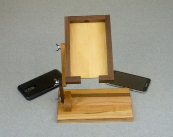 May include: A wooden phone stand with a walnut frame and a light wood base. The stand has two adjustable arms that can be used to hold a phone in portrait or landscape mode.