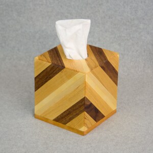 Peut inclure: Un porte-mouchoirs en bois avec un motif géométrique en bois clair et foncé. La boîte est faite de différents types de bois, dont le noyer et l'érable.