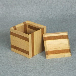 May include: A wooden box with a striped pattern in shades of brown and beige. The box is open and the lid is lying next to it.
