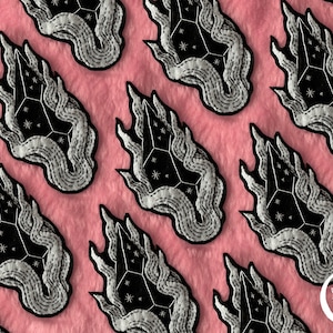 May include: A repeating pattern of embroidered patches featuring a black crystal with white stars and a silver-grey flame design. The patches are on a pink fuzzy background.