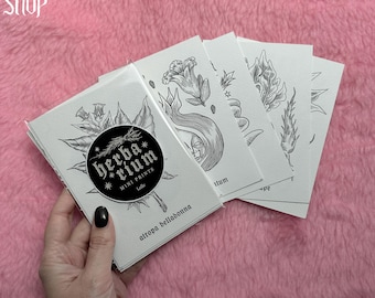 Op de afbeelding: Een stapel witte mini-prints met botanische illustraties en de tekst "herba*rium MINI PRINTS Lolle". De prints worden in een hand gehouden tegen een roze, pluizige achtergrond. De prints bevatten afbeeldingen van bloemen, bladeren en een gezicht.