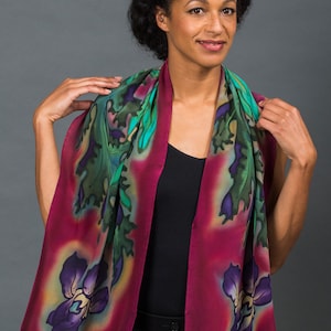 May include: A woman wearing a black top and black trousers is wearing a long, burgundy silk scarf with green and purple floral designs.