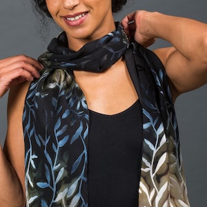 May include: A black scarf with a leaf pattern in shades of blue, green, and white. The scarf is draped around the neck and shoulders. The scarf's design features a repeating pattern of stylized leaves.