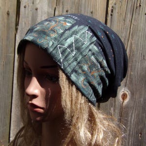 May include: A dark blue beanie hat with a green and white abstract design. The hat has a folded brim and is made of a soft, stretchy fabric. The design features geometric shapes and orange accents.
