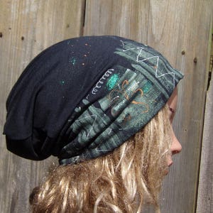 May include: A black beanie with a patterned design in shades of green and white. The beanie has a unique design with white stitching and a splash of glitter. The hat is made of a soft material.