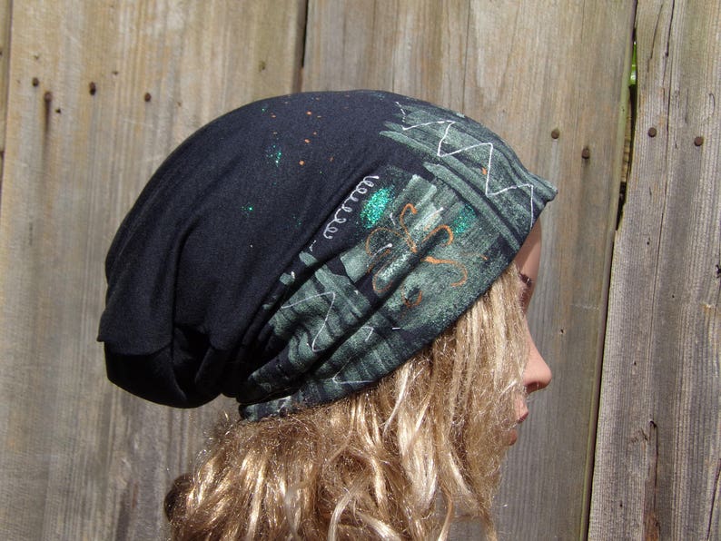 May include: A black beanie with a patterned design in shades of green and white. The beanie has a unique design with white stitching and a splash of glitter. The hat is made of a soft material.