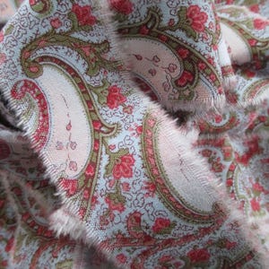 Peut inclure: Gros plan sur un tissu à motif paisley dans les tons rose, bleu et vert. Le tissu a un bord effiloché.