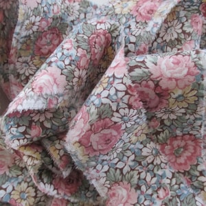 May include: A close-up of a fabric with a floral pattern. The fabric is a mix of pink, white, and green flowers on a brown background.