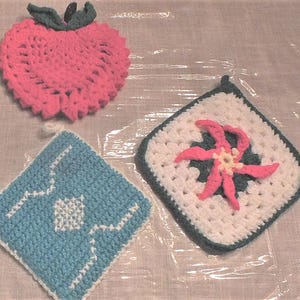 May include: Four crocheted pot holders in different designs. One is a pink heart shape, one is a blue and white geometric design, one is a white and green snowflake design, and one is a white and pink flower design.