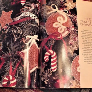 May include: A book titled "The Tastes of Christmas" with a red and white candy cane, a red and white star, and a red and white ornament on the cover. The book is open to a page with a close-up of the ornaments.