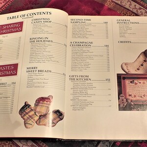 May include: Open book with a table of contents for a Christmas cookbook. The book features recipes for a variety of Christmas dishes, including sweet breads, candy, and cocktails. The book also includes instructions for making Christmas crafts.