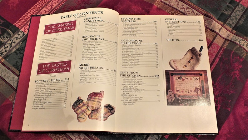 May include: Open book with a table of contents for a Christmas cookbook. The book features recipes for a variety of Christmas dishes, including sweet breads, candy, and cocktails. The book also includes instructions for making Christmas crafts.