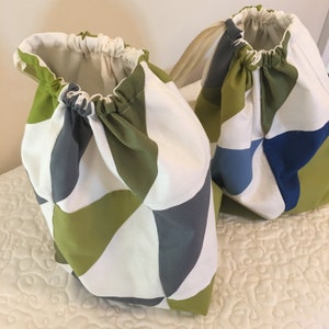 Può includere: Due sacche a cordoncino in tessuto con un motivo geometrico in tonalità di verde, bianco e grigio. Una borsa ha un motivo blu e grigio.