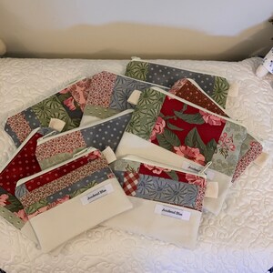 Puede incluir: Una pila de ocho peque&ntilde;as bolsas con cremallera hechas de tela de patchwork en tonos de rojo, verde, azul y blanco. Las bolsas tienen un forro blanco y un tirador de cremallera blanco. Las bolsas est&aacute;n etiquetadas con "Accidental Bliss".