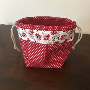 Op de afbeelding: Rode en witte trekkoordtas met een bloemenprint en stippenpatroon. De tas heeft één compartiment en een trekkoord sluiting.