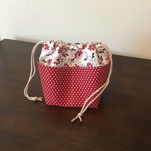 Op de afbeelding: Een rode en witte trekkoordtas met een bloemenprint. De tas is gemaakt van stof en heeft een wit trekkoord.