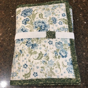 May include: A white fabric storage case with a green border and a blue floral pattern. The case has a white strap with a green buckle.