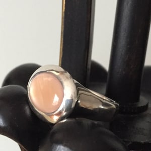 Puede incluir: Un anillo de plata con una piedra preciosa grande, ovalada, de color rosa claro.