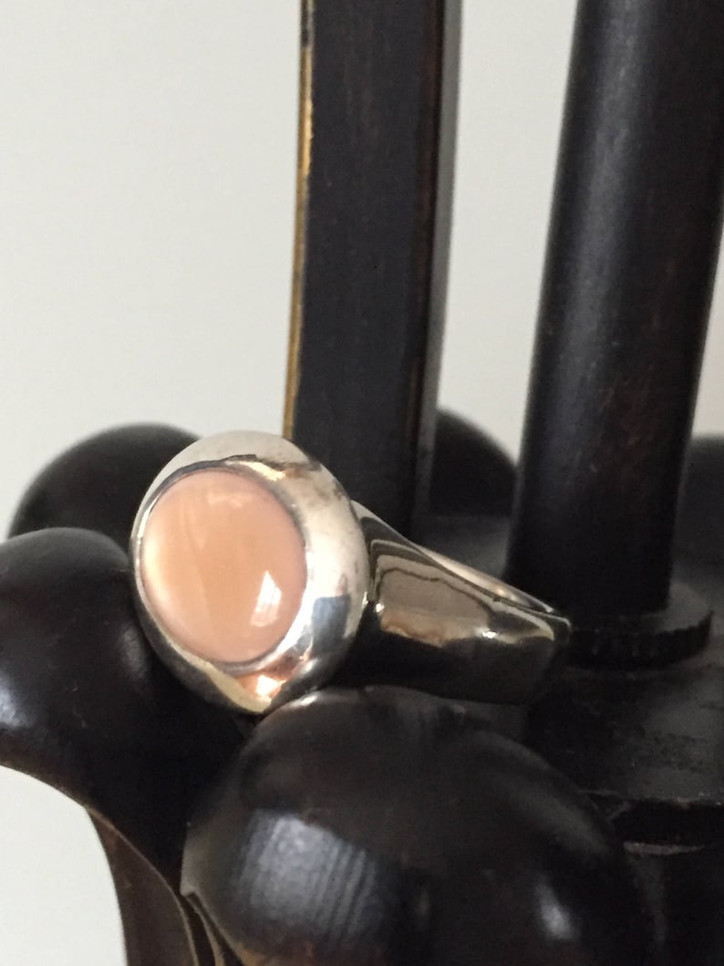 Puede incluir: Un anillo de plata con una piedra preciosa grande, ovalada, de color rosa claro.