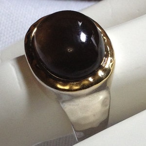 May include: A silver ring with a gold band and a large, dark brown oval gemstone.