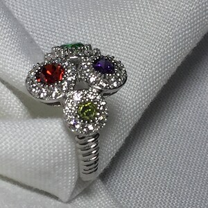 May include: A silver ring with four colorful gemstones set in a halo of smaller stones. The ring has a twisted band.