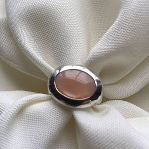 Puede incluir: Un anillo de plata con una piedra ovalada de color rosa claro engastada en un engaste de bisel.