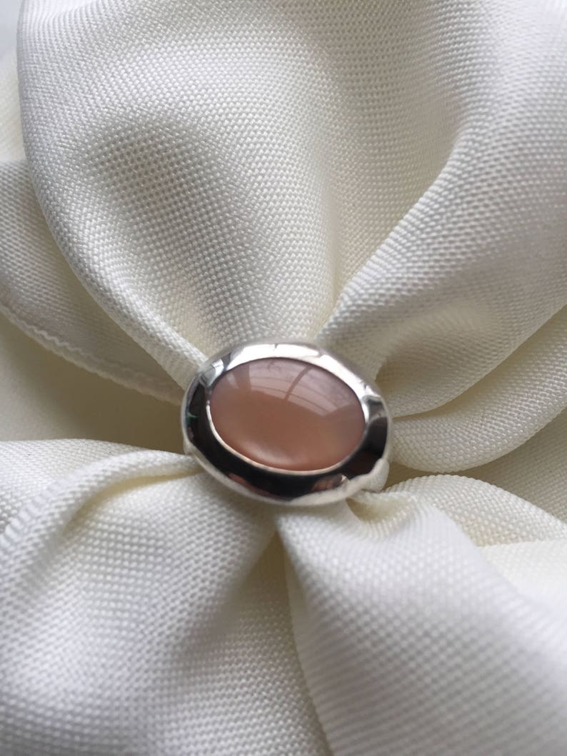 Puede incluir: Un anillo de plata con una piedra ovalada de color rosa claro engastada en un engaste de bisel.