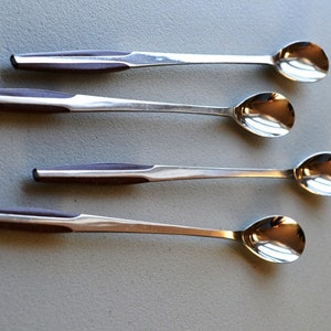 May include: Four silver spoons with teardrop-shaped bowls and dark brown wooden handles are arranged diagonally on a gray surface. The spoons are reflective, and the handles have a rectangular shape.