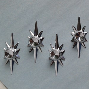 May include: Six silver starburst-shaped cabinet knobs with a raised center circle. The knobs are arranged in a row on a light blue surface.