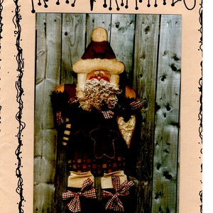 May include: A handmade felt Christmas cookie Santa ornament with a red and white plaid pattern, a brown felt hat, and a white felt beard. The ornament is hanging on a wooden background. The text "Cookie Santa #8" is printed below the ornament.
