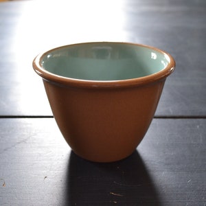 May include: A brown ceramic cup with a light blue interior. The cup is sitting on a dark wooden table.