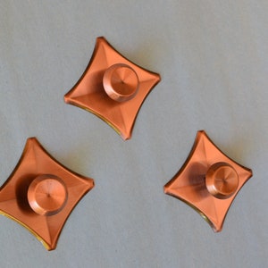 May include: Four copper-colored, star-shaped cabinet knobs with a raised, round center.