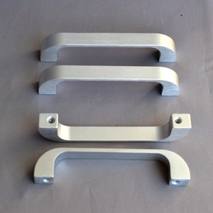 May include: Four silver cabinet pulls with a rounded rectangular shape. The pulls are different sizes.