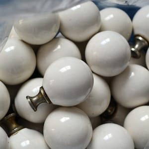 May include: A close-up of a bag filled with white ceramic round knobs with silver metal bases. The knobs are arranged in a random pattern.