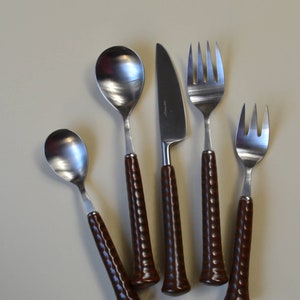 May include: A set of five silver-toned cutlery pieces with brown wooden handles. The set includes a knife, two spoons, and two forks.